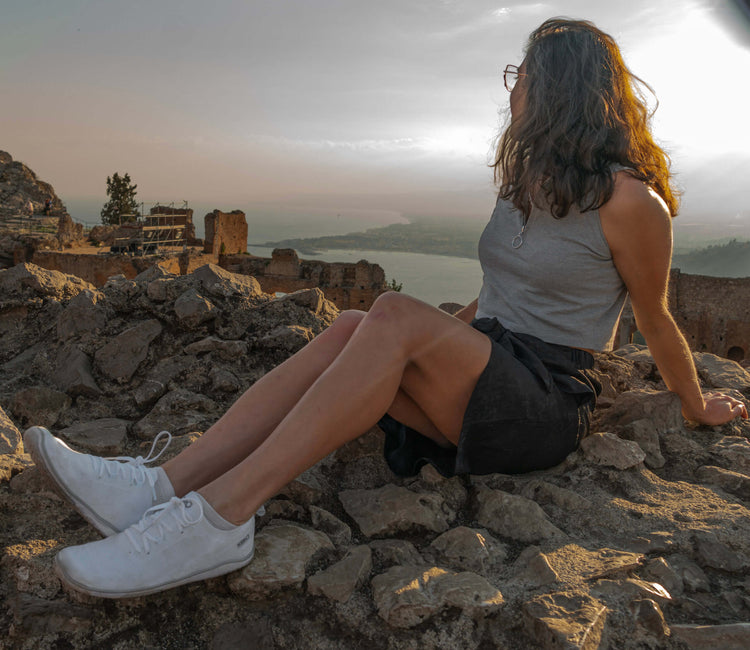 Woman laying on rocks wearing Xero Shoes in Italy enjoying a high up view